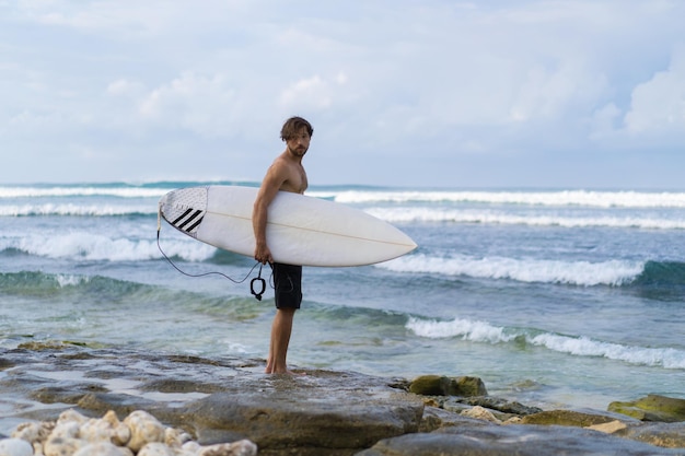 Hombre guapo joven con una tabla de surf en el océano.