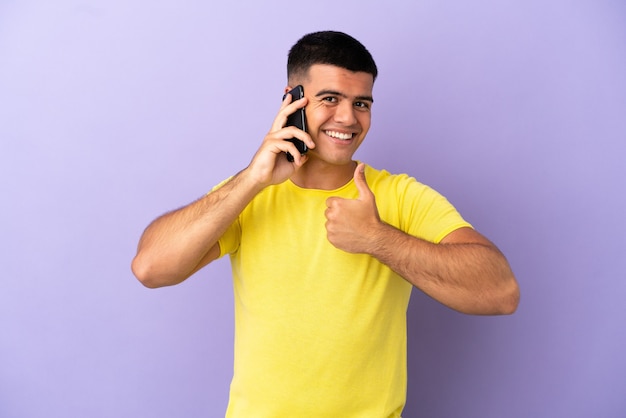 Hombre guapo joven con teléfono móvil sobre fondo púrpura aislado dando un pulgar hacia arriba gesto