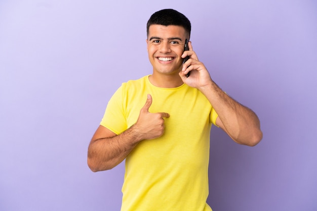 Hombre guapo joven con teléfono móvil sobre fondo púrpura aislado con expresión facial sorpresa