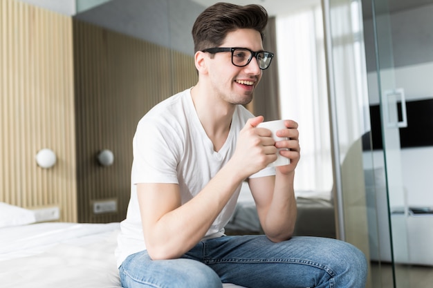 Hombre guapo joven tomando café en la cama