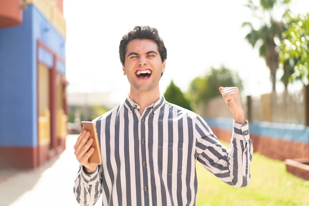 Hombre guapo joven usando teléfono móvil y haciendo gesto de victoria