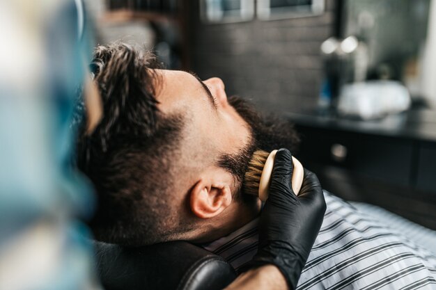 Hombre guapo joven visitando peluquería. Corte y peinado de barba a la moda y con estilo.