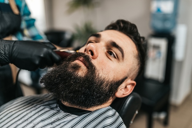 Hombre guapo joven visitando peluquería. Corte y peinado de barba a la moda y con estilo.