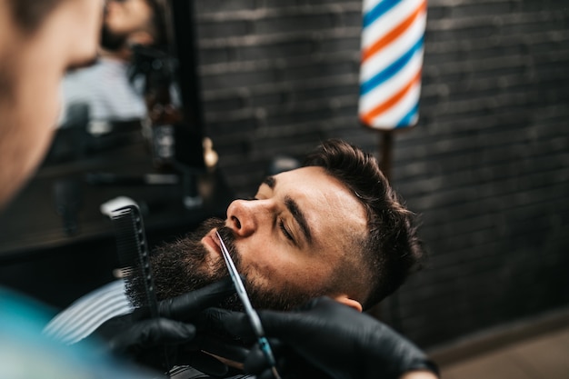 Hombre guapo joven visitando peluquería. Corte y peinado de barba a la moda y con estilo.