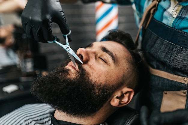 Hombre guapo joven visitando peluquería. Corte y peinado de barba a la moda y con estilo.