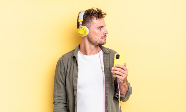 Hombre guapo joven en vista de perfil pensando imaginando o soñando auriculares y concepto de teléfono inteligente