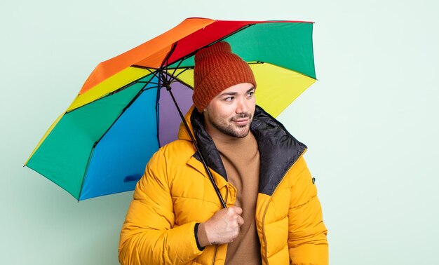 Hombre guapo joven en vista de perfil pensando, imaginando o soñando despierto. concepto de lluvia y paraguas