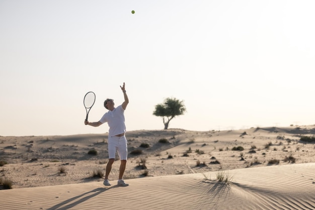 Hombre guapo jugando tenis en un barkhan en el desierto