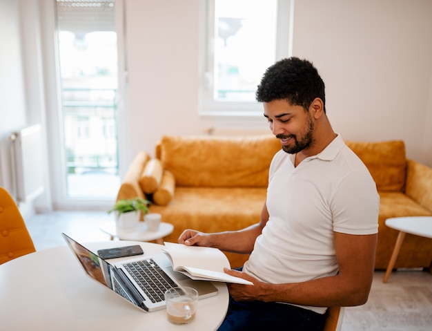 Hombre guapo con laptop y libro en casa.