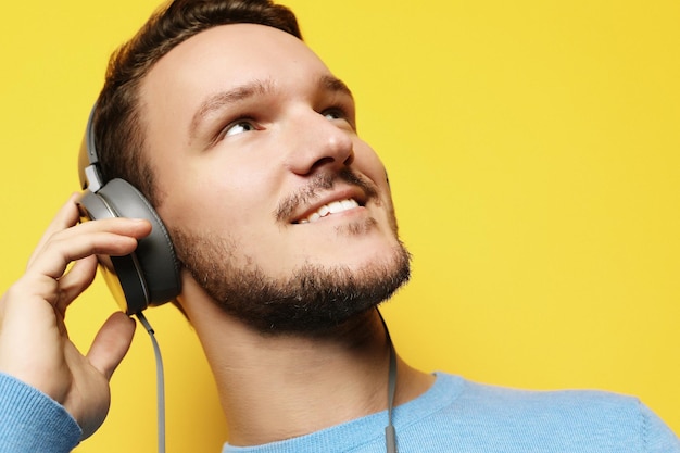 Hombre guapo licuando a la música sobre fondo amarillo