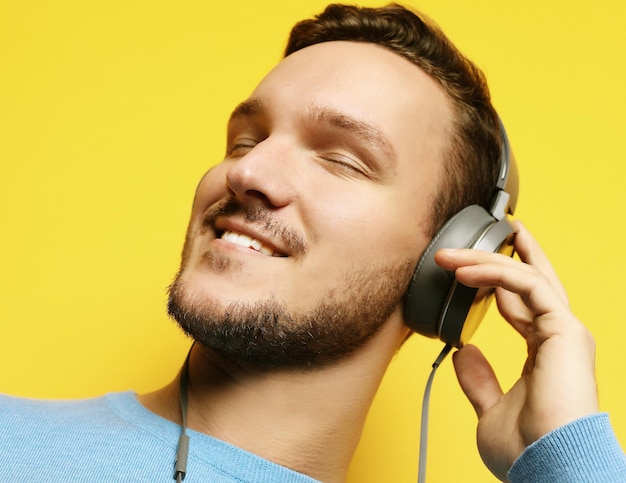 Hombre guapo licuando a la música sobre fondo amarillo