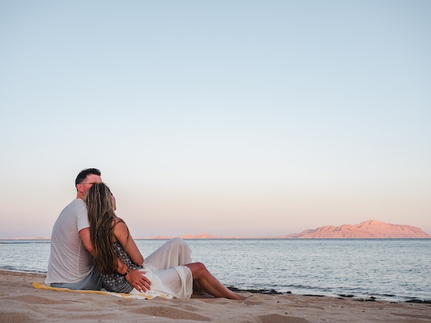 Hombre guapo y linda mujer sentada en la playa