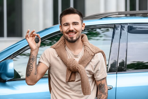 Hombre guapo con llave de coche cerca de coche moderno