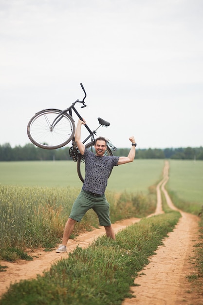 Hombre guapo lleva su bicicleta a pie por un camino de campo