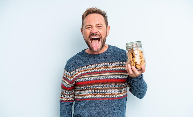 Hombre guapo de mediana edad con actitud alegre y rebelde, bromeando y sacando la lengua. botella de galletas