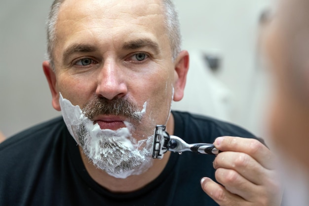 Hombre guapo de mediana edad afeitándose la barba en el baño.