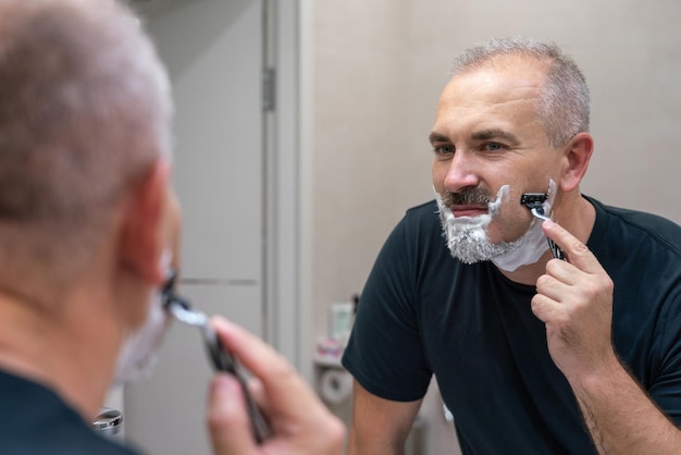 Hombre guapo de mediana edad afeitándose la barba en el baño.