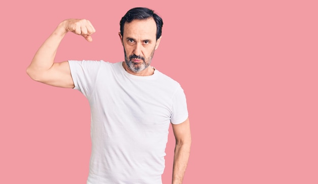Hombre guapo de mediana edad con camiseta casual persona fuerte mostrando músculo del brazo seguro y orgulloso del poder