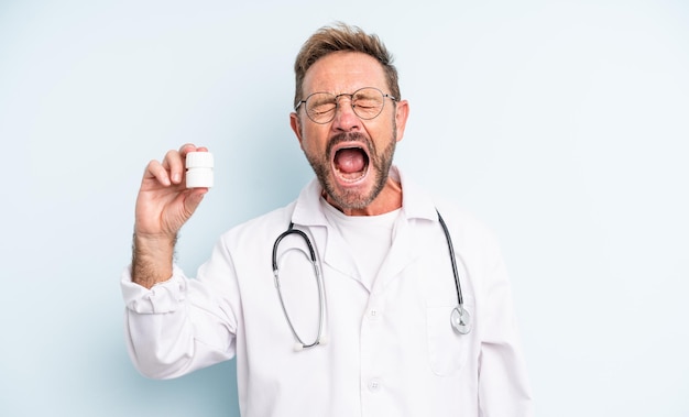 Hombre guapo de mediana edad gritando agresivamente mirando a un médico muy enojado con una botella de pastillas