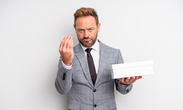 Hombre guapo de mediana edad haciendo capice o gesto de dinero, diciéndole que pague. concepto de paquete blanco