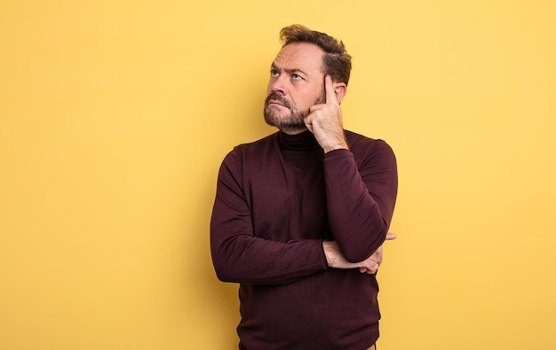 Hombre guapo de mediana edad con una mirada concentrada, preguntándose con una expresión dudosa, mirando hacia arriba y hacia un lado.