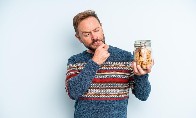 Hombre guapo de mediana edad pensando, sintiéndose dudoso y confundido. botella de galletas