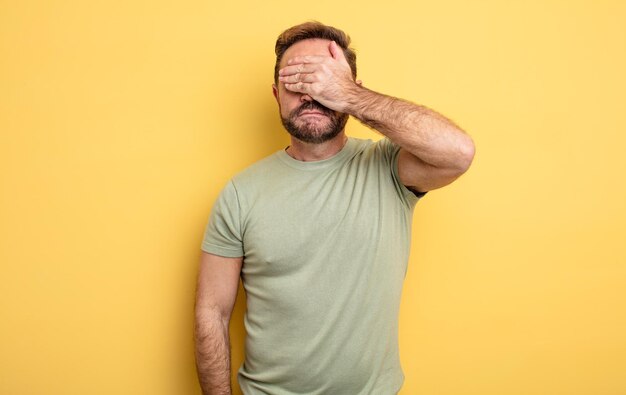 Hombre guapo de mediana edad que cubre los ojos con una mano sintiéndose asustado o ansioso, preguntándose o esperando ciegamente una sorpresa