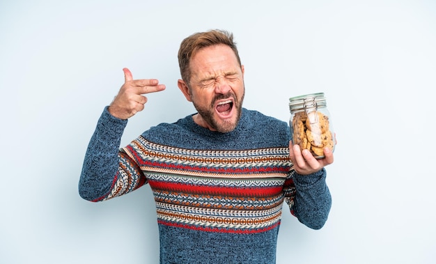 Hombre guapo de mediana edad que parece infeliz y estresado, gesto de suicidio haciendo señas de armas. botella de galletas