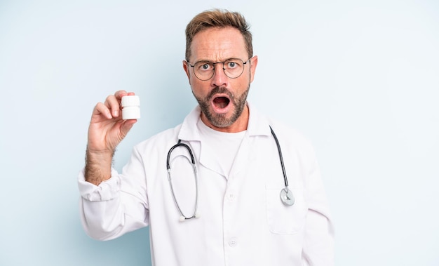 Hombre guapo de mediana edad que parece muy conmocionado o sorprendido. médico con botella de pastillas