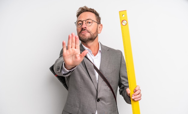 Hombre guapo de mediana edad que parece serio mostrando la palma abierta haciendo gesto de parada. concepto de arquitecto