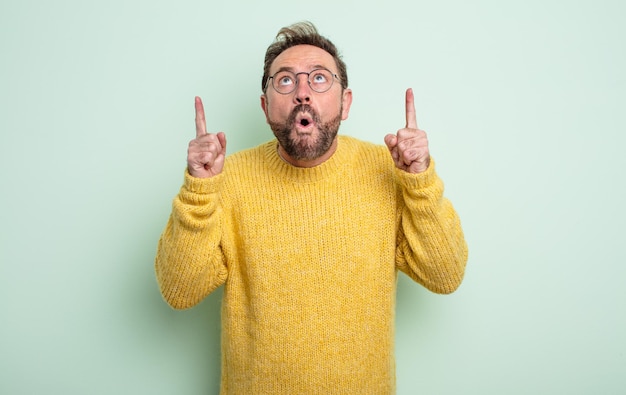 Hombre guapo de mediana edad que se siente asombrado y con la boca abierta apuntando hacia arriba con una mirada conmocionada y sorprendida