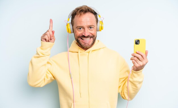 Hombre guapo de mediana edad que se siente como un genio feliz y emocionado después de darse cuenta de una idea de concepto de auriculares y teléfono inteligente