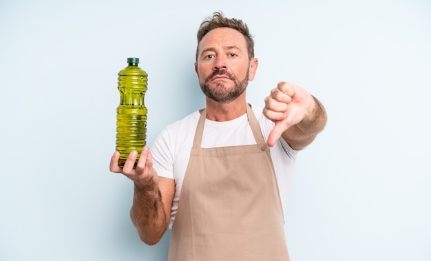 Hombre guapo de mediana edad que se siente cruzado, mostrando los pulgares hacia abajo. concepto de aceite de oliva