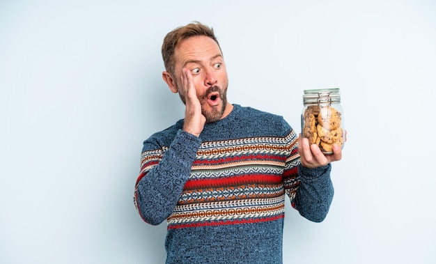 Hombre guapo de mediana edad que se siente feliz emocionado y sorprendido botella de galletas