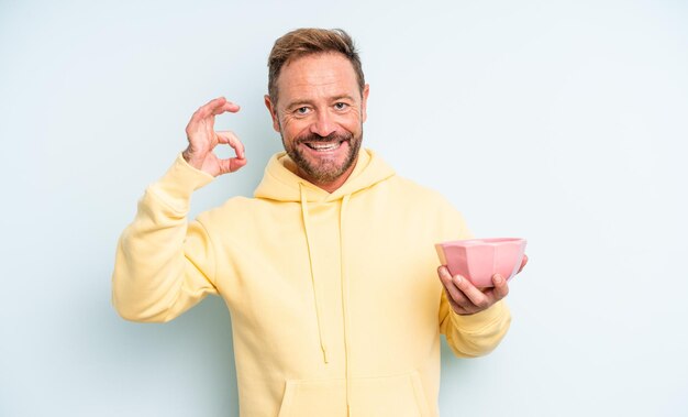 Hombre guapo de mediana edad que se siente feliz, mostrando aprobación con un gesto correcto. concepto de tazón vacío