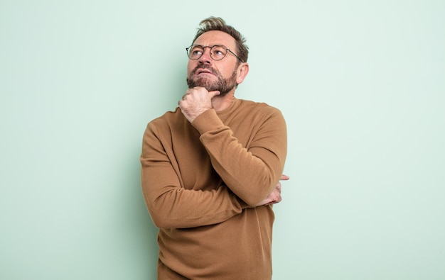 Hombre guapo de mediana edad que se siente pensativo, preguntándose o imaginando ideas, soñando despierto y mirando hacia arriba para copiar espacio