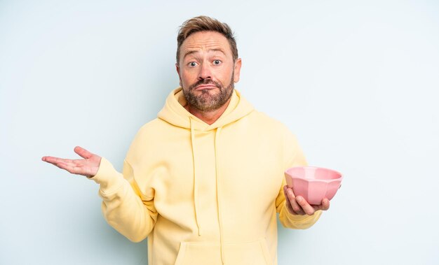 Hombre guapo de mediana edad que se siente perplejo y confundido y que duda del concepto de tazón vacío