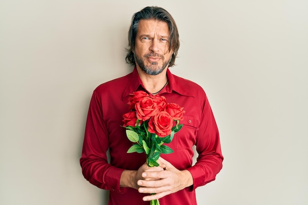 Hombre guapo de mediana edad con ramo de rosas rojas concepto de duda de expresión despistada y confusa