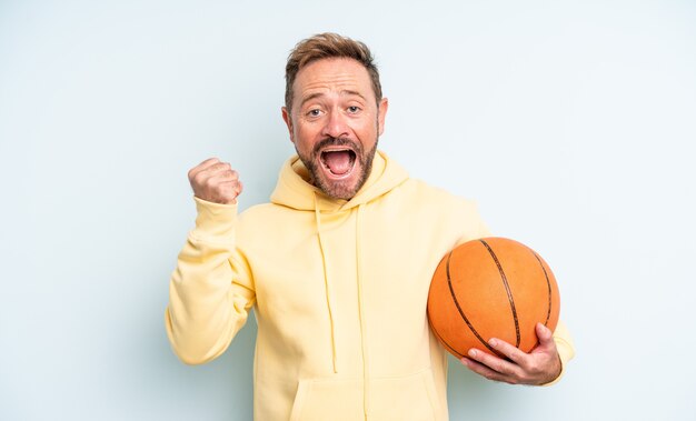 Hombre guapo de mediana edad sintiéndose conmocionado, riendo y celebrando el éxito. concepto de baloncesto