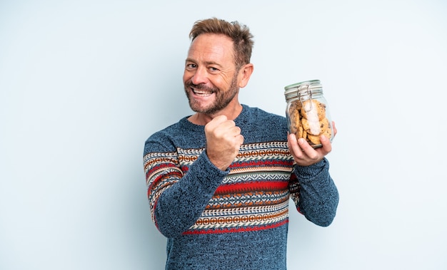 Hombre guapo de mediana edad sintiéndose feliz y enfrentando un desafío o celebrando. botella de galletas