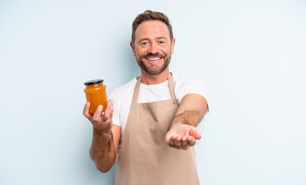 Hombre guapo de mediana edad sonriendo felizmente con amable y ofreciendo y mostrando un concepto. concepto de mermelada de durazno