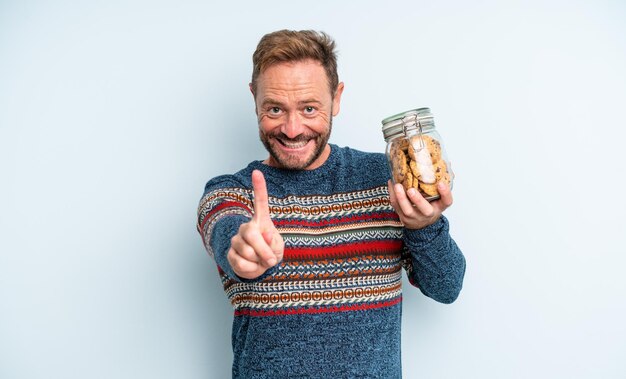 Hombre guapo de mediana edad sonriendo con orgullo y confianza haciendo el número uno. botella de galletas