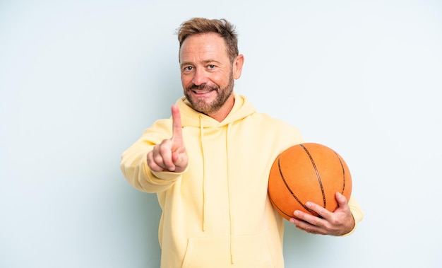 Hombre guapo de mediana edad sonriendo con orgullo y confianza haciendo el número uno. concepto de baloncesto