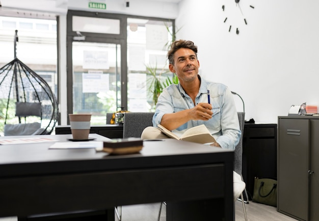 Foto hombre guapo, de mediana edad, en el trabajo, oficina, sentado sosteniendo una pluma