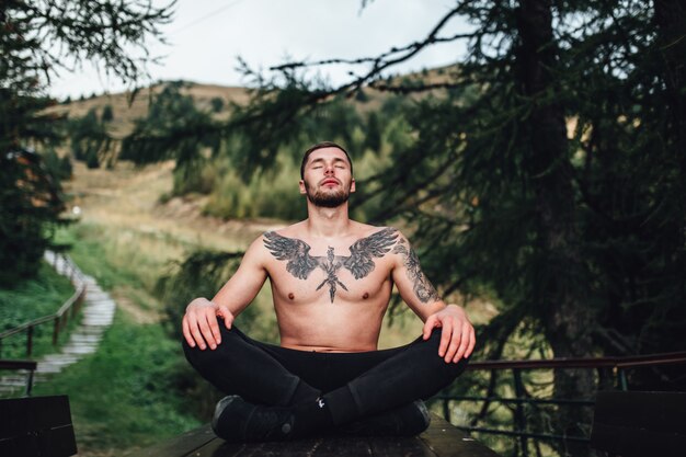 Hombre guapo meditando sobre la mesa en el bosque