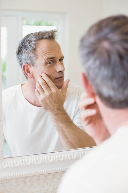 Hombre guapo mirando a sí mismo en el espejo en el baño