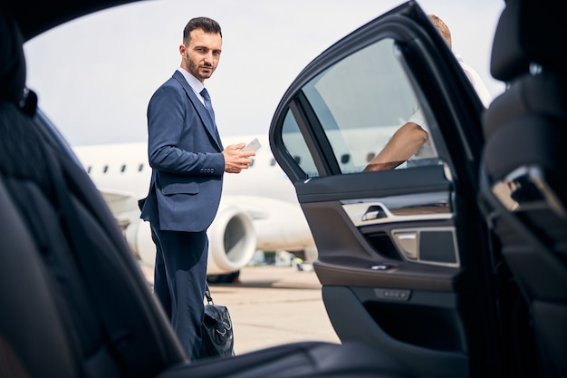 Foto hombre guapo morena con un elegante traje sosteniendo su equipaje de mano junto a un taxi