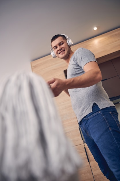 Hombre guapo morena con grandes auriculares apuntando a la cámara fotográfica con paño de piso y riendo