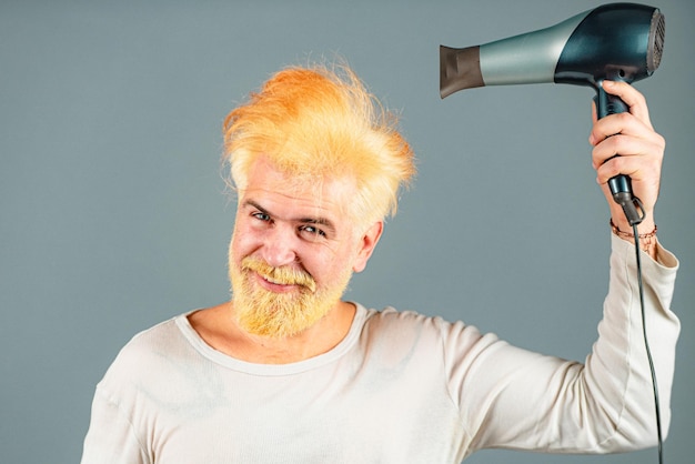 Hombre guapo pelirrojo con cabello largo se seca el cabello con un secador de pelo. Hombre rubio con secador de pelo.