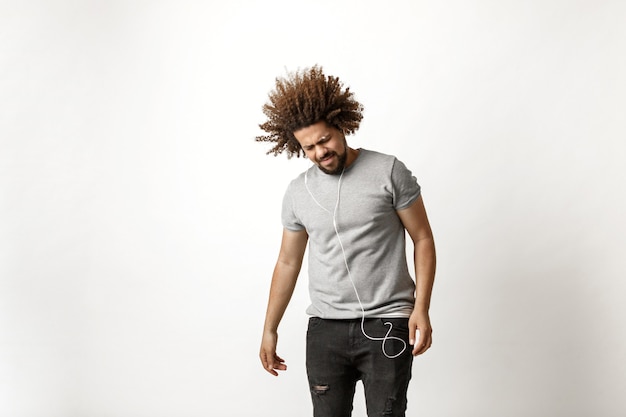 un hombre guapo de pelo rizado con una camiseta gris y jeans rotos está escuchando música